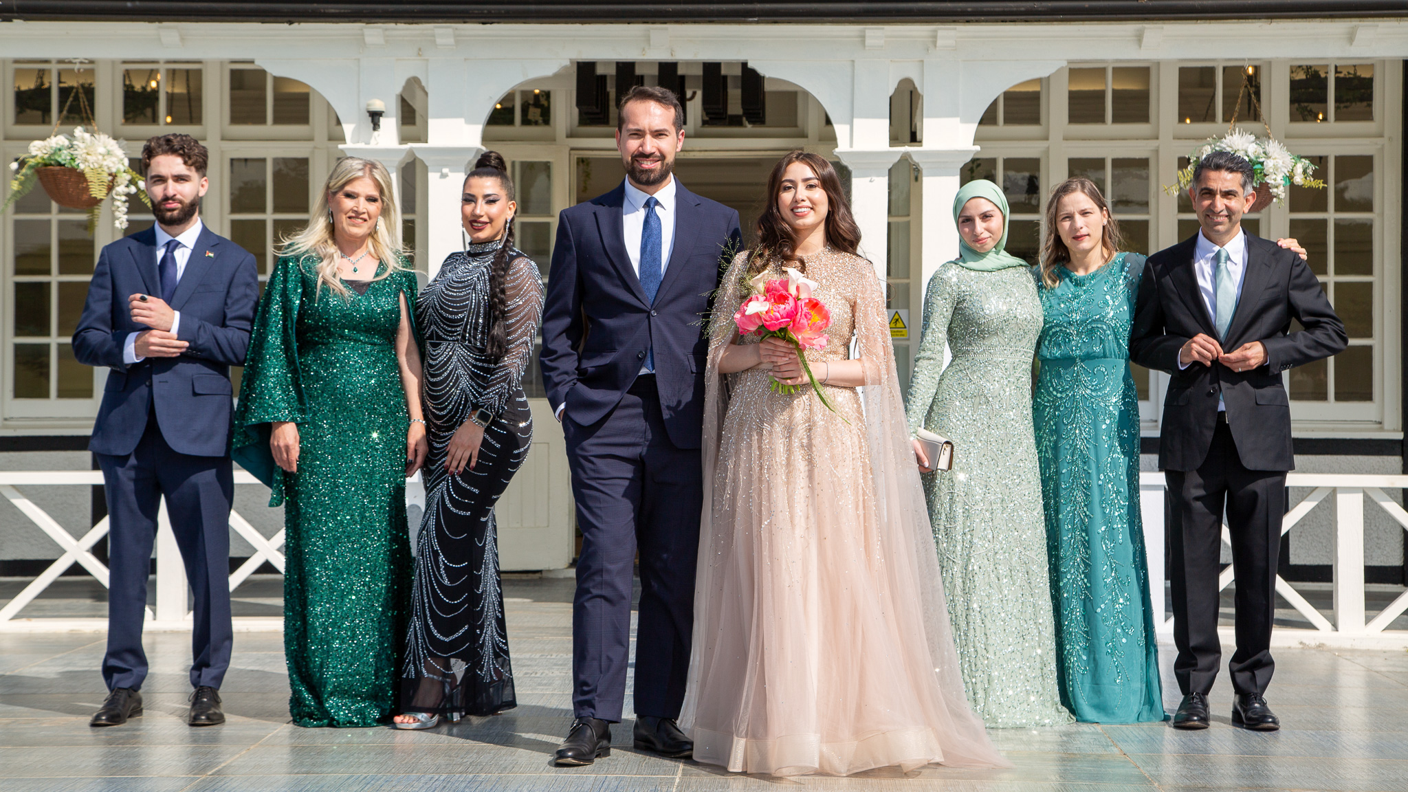 Elegant wedding group photo captured by INSE Photography in Surrey, featuring the bride, groom, and family dressed in formal attire outside a bright white venue. Professional wedding photography by a female photographer in Surrey and London.